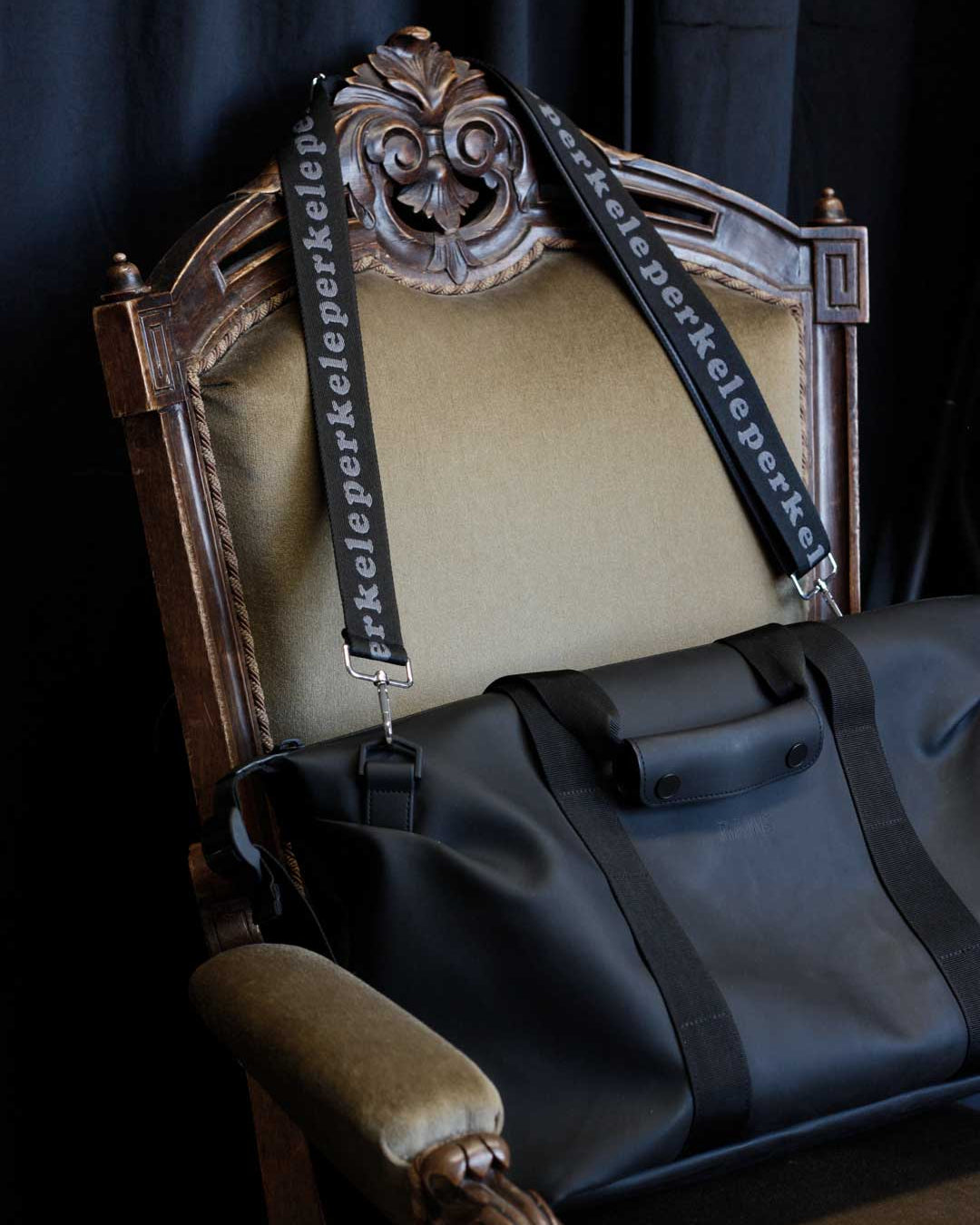 Black bag with a decorative strap on an ornate chair against a dark background