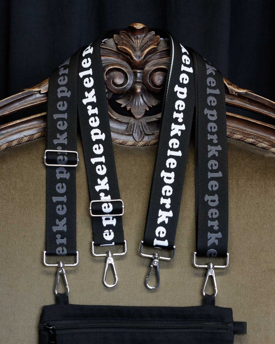 Black straps with 'perkele' text hanging on a decorative chair.