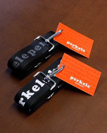 Two black keychains with silver clips on a brown surface, each accompanied by an orange card displaying 'perkele'.