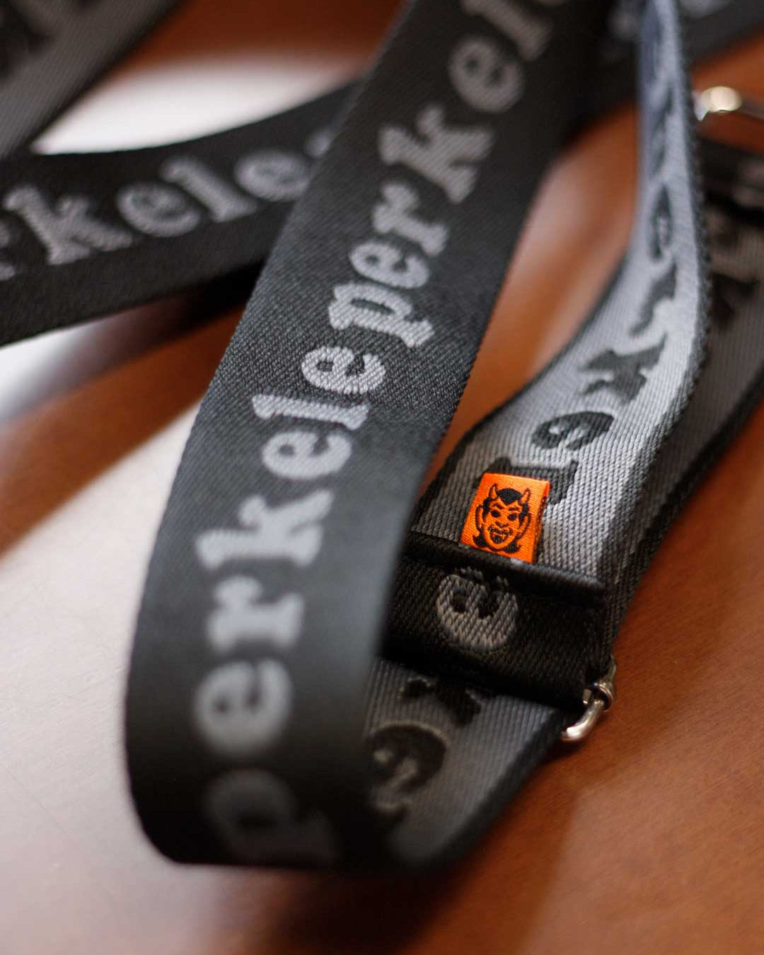 Close-up of a Perkele purse strap with brand name perkele and small orange devil logo.
